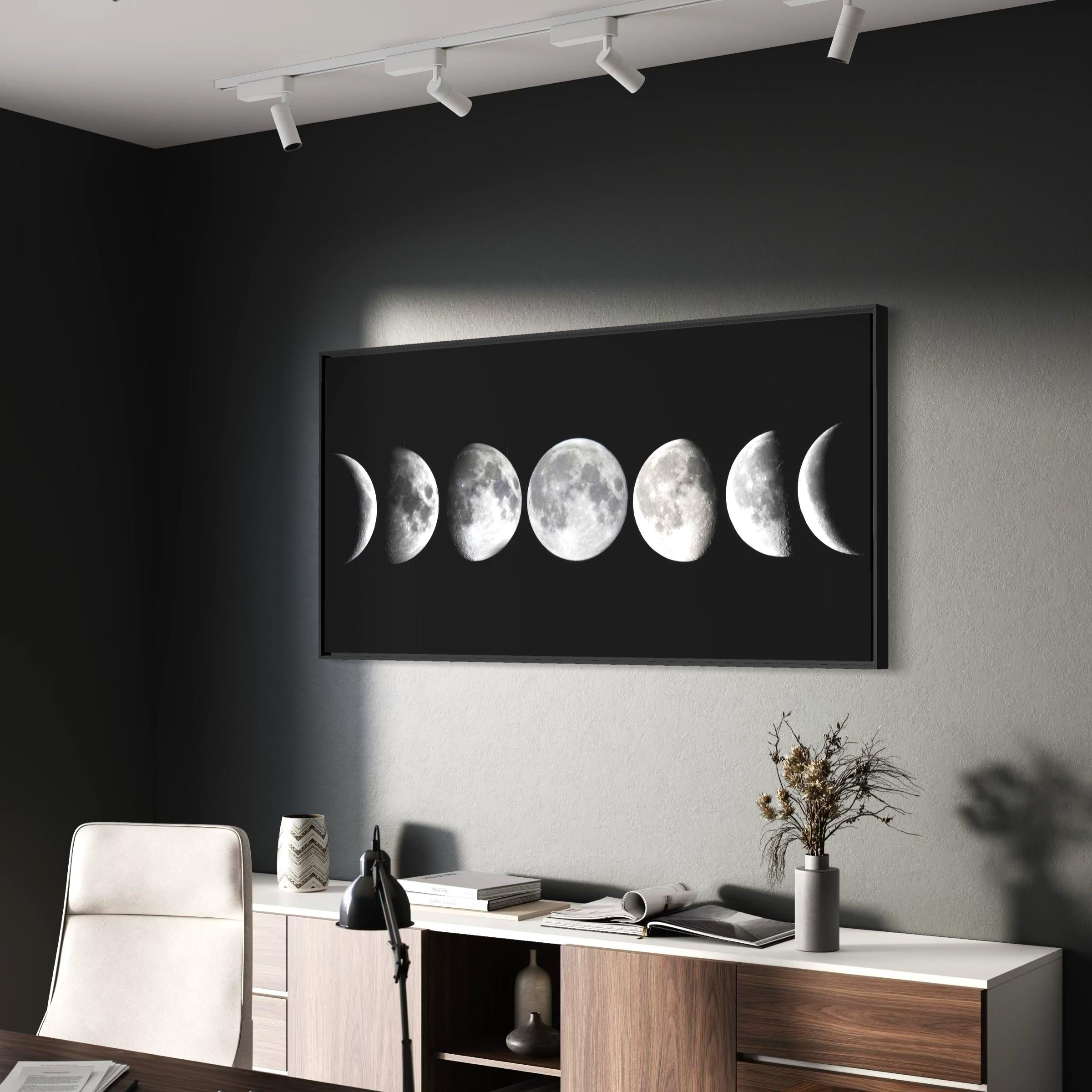 May include: A framed black and white print featuring the phases of the moon. The artwork shows the moon's progression from crescent to full and back, set against a black background. The print is displayed in a modern office setting.