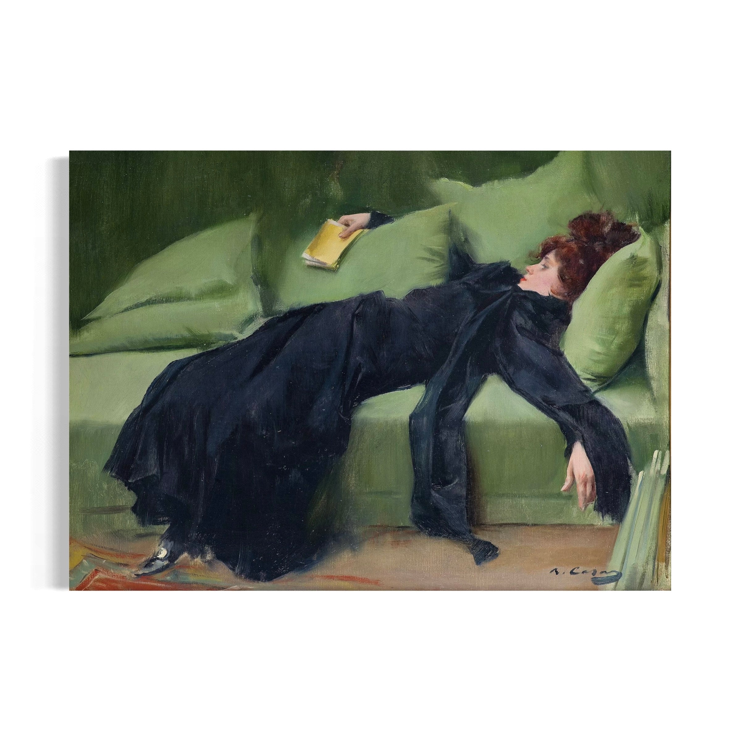 A woman in a black dress is lying on a green couch, holding a book in her hand.